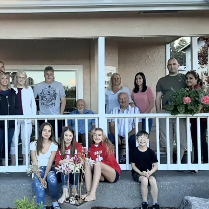 A multi-generational family poses for a group portrait on the front porch of a house.