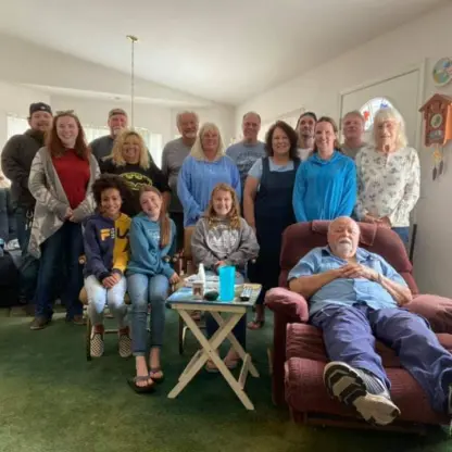 A large family group posing for a photo in a living room, with an elderly man resting in a recliner in the foreground.