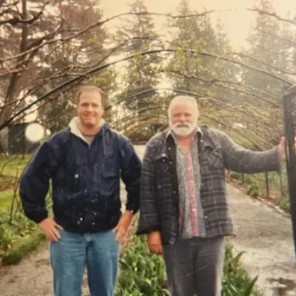 Two men stand together under a metal garden archway.