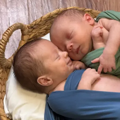 Two newborns swaddled in green and blue fabric sleeping in a woven basket.