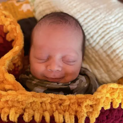A sleeping newborn baby bundled in a thick, textured, multi-colored yarn blanket.