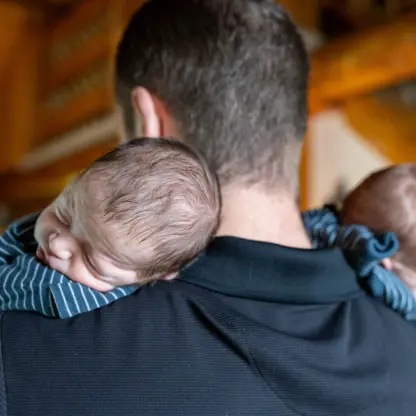 A man holds two sleeping newborns over his shoulders.