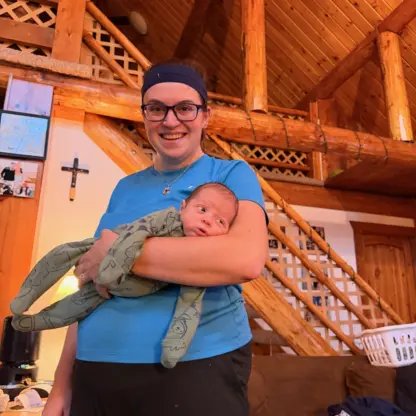 A woman smiling while holding a newborn baby in a log cabin.