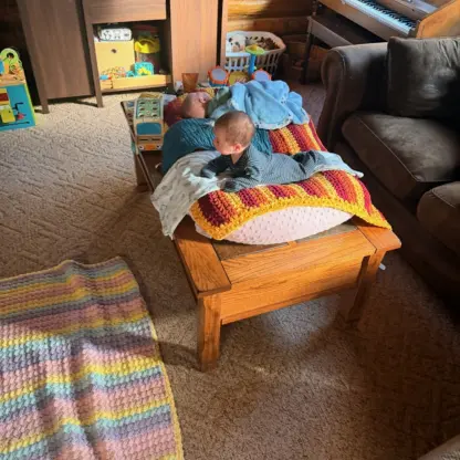 Two infants lie on a wooden coffee table covered with blankets.