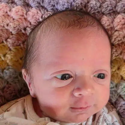 A close-up portrait of a newborn baby lying on a textured, multi-colored crocheted blanket.