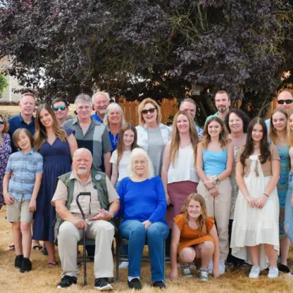 A large multi-generational family poses for a group portrait outdoors in front of a tree.
