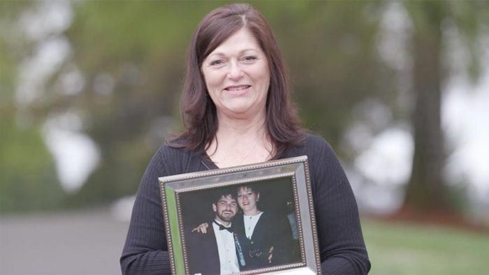 Woman smiles at cemetery and holds up photo of deceased loved one