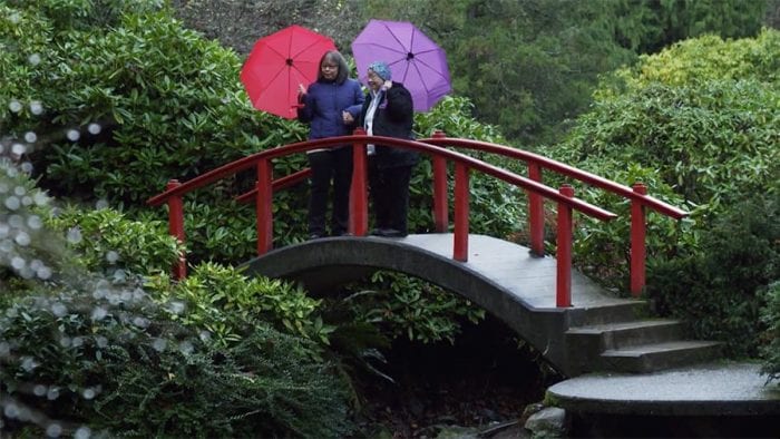 Two women with umbrellas on bridge in green garden in Seattle