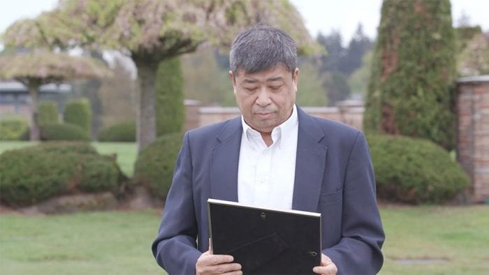 Man in cemetery looks pensively down at framed photo of deceased loved one