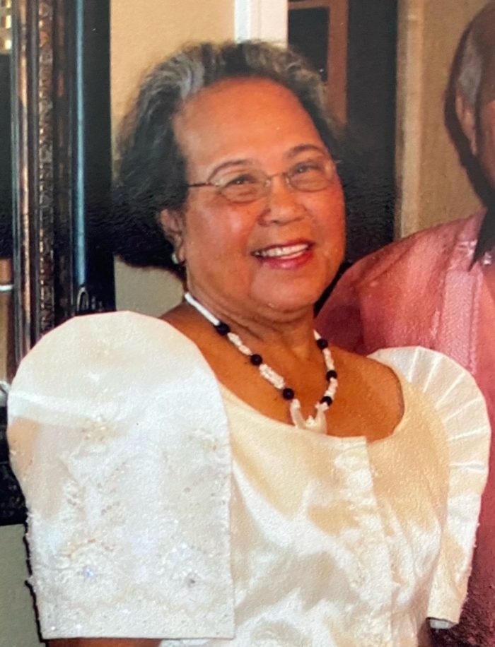 a woman wearing a white dress, beaded necklace, and glasses smiles