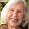 a woman, with tinted lipstick and silver hair cut in a bob, smiles brightly