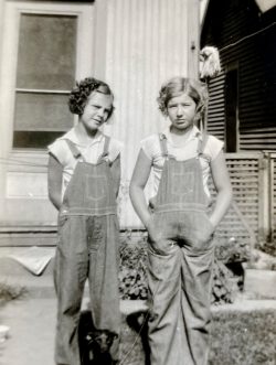 two young girls wearing overalls in front of a house